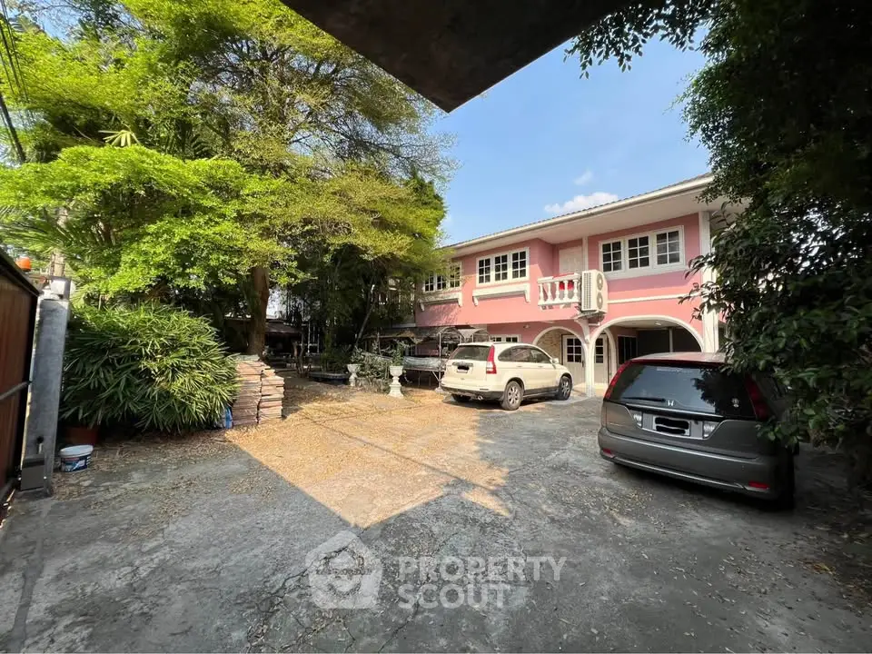 Charming pink two-story house with spacious driveway and lush greenery