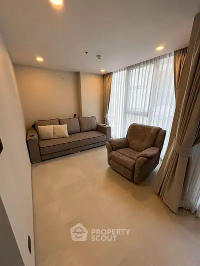 Cozy living room with modern sofa and armchair, featuring floor-to-ceiling windows and elegant curtains.
