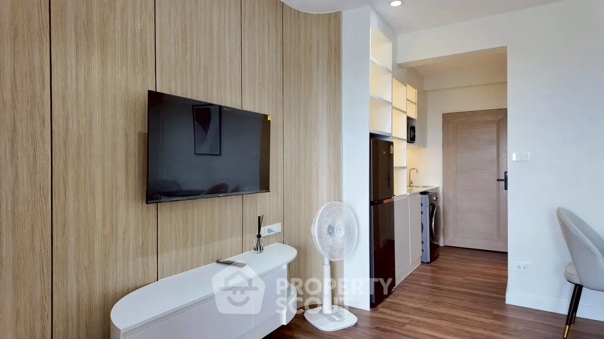 Modern living room with sleek TV and stylish wooden paneling, open kitchen layout, and elegant flooring.