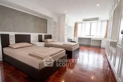 Spacious twin bedroom with elegant wooden flooring and ample natural light.
