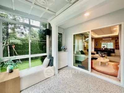 Spacious living room with large windows overlooking a lush garden, featuring modern decor and cozy seating.