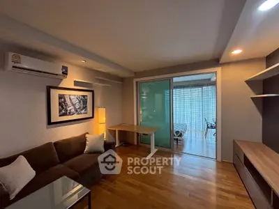 Modern living room with wooden flooring, cozy sofa, and sliding glass doors leading to a balcony.