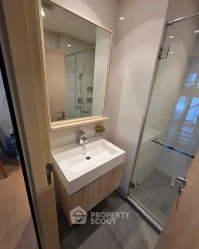 Modern bathroom with sleek vanity and glass shower enclosure in contemporary apartment.