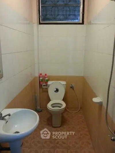Compact bathroom with tiled floor, toilet, sink, and shower area.