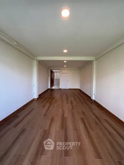 Spacious empty room with wooden flooring and bright lighting, perfect for customization.