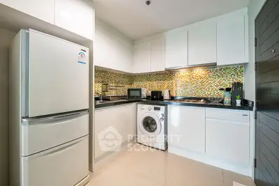 Modern kitchen with sleek white cabinets, washing machine, and mosaic backsplash in a compact layout.