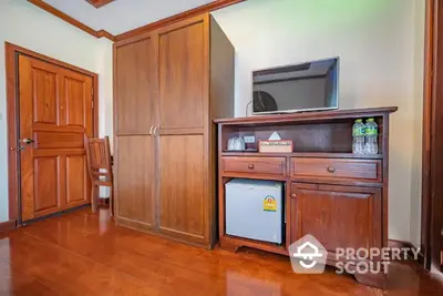 Cozy room corner featuring polished wooden floors, a classic wooden wardrobe, and a TV cabinet with a mini-fridge, radiating a warm, homely atmosphere.