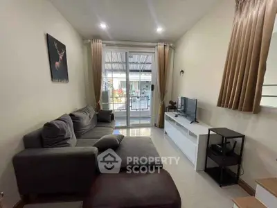 Cozy living room with modern sofa and TV, bright natural light through large windows.