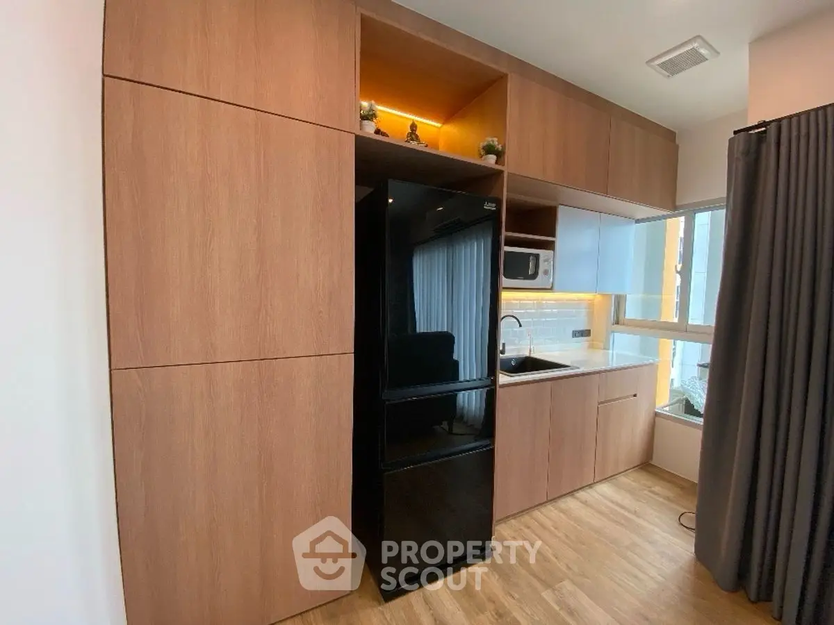 Modern kitchen with sleek black fridge and wooden cabinetry in stylish apartment.