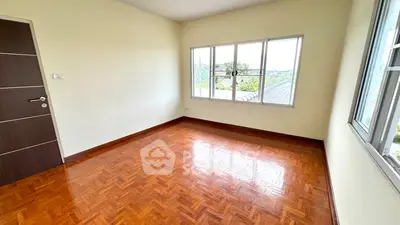Spacious empty room with polished wooden floors and large windows offering natural light.