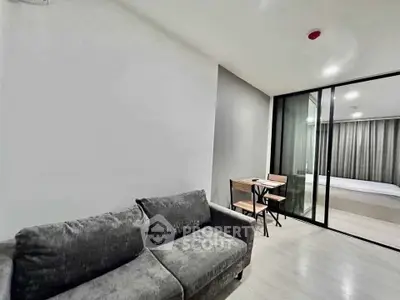 Modern living room with cozy gray sofa and glass partition to bedroom.