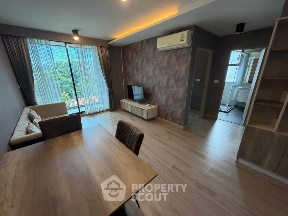 Modern living room with wooden flooring, stylish furniture, and large windows offering a scenic view.