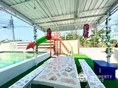 Charming outdoor pool area with covered seating and playful slide, perfect for family gatherings.