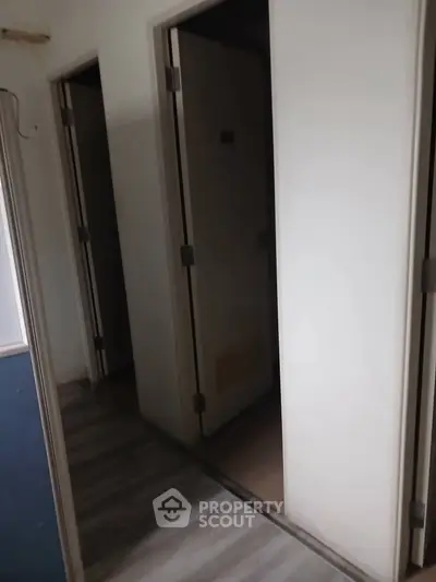 Dimly lit hallway with closed doors and wooden flooring, ideal for storage or utility space.