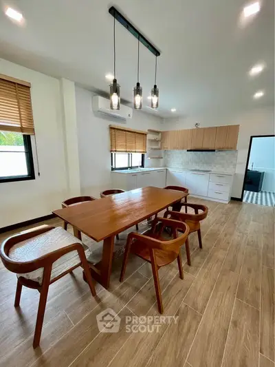 Modern dining area with wooden table and chairs, open kitchen layout, and stylish lighting.