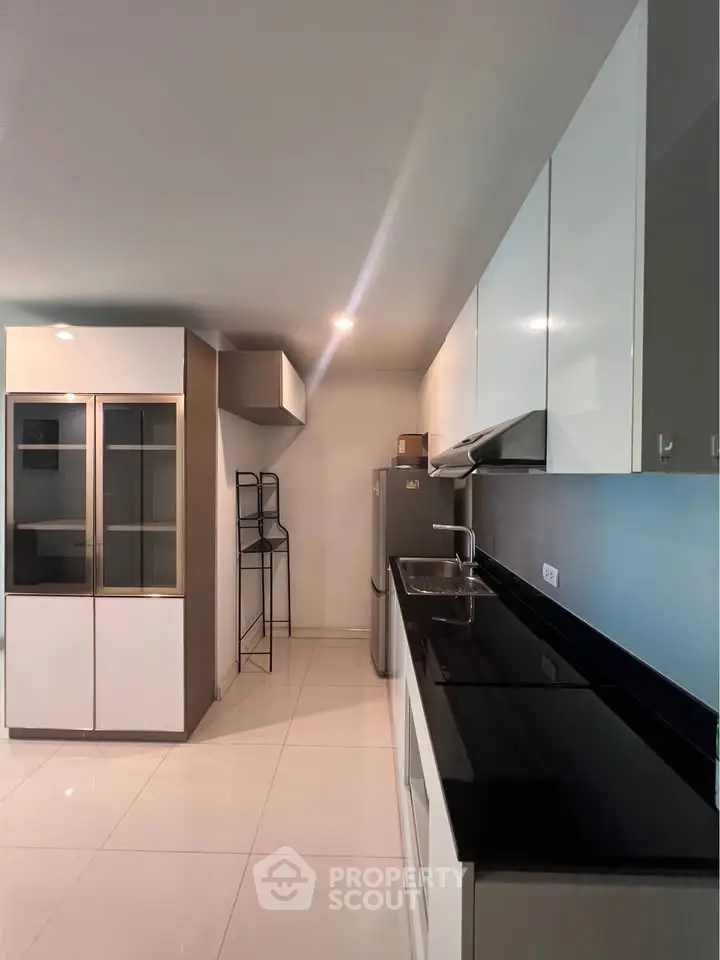 Modern kitchen with sleek black countertops and white cabinetry, featuring a stainless steel fridge and ample storage.