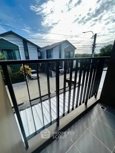 Charming balcony with modern railing overlooking suburban street and houses under a bright sky.