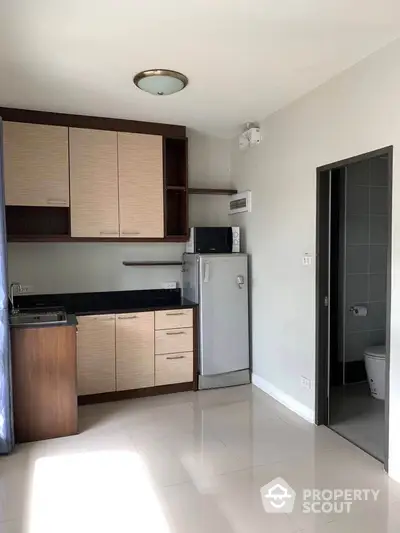 Compact kitchen with modern cabinets, mini fridge, and microwave adjacent to a bathroom entrance.