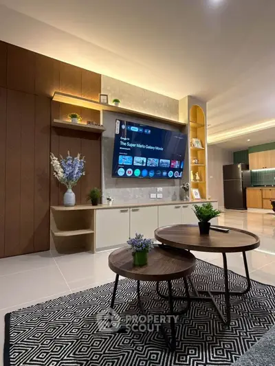 Modern living room with stylish decor and open kitchen layout, featuring a wall-mounted TV and elegant furniture.