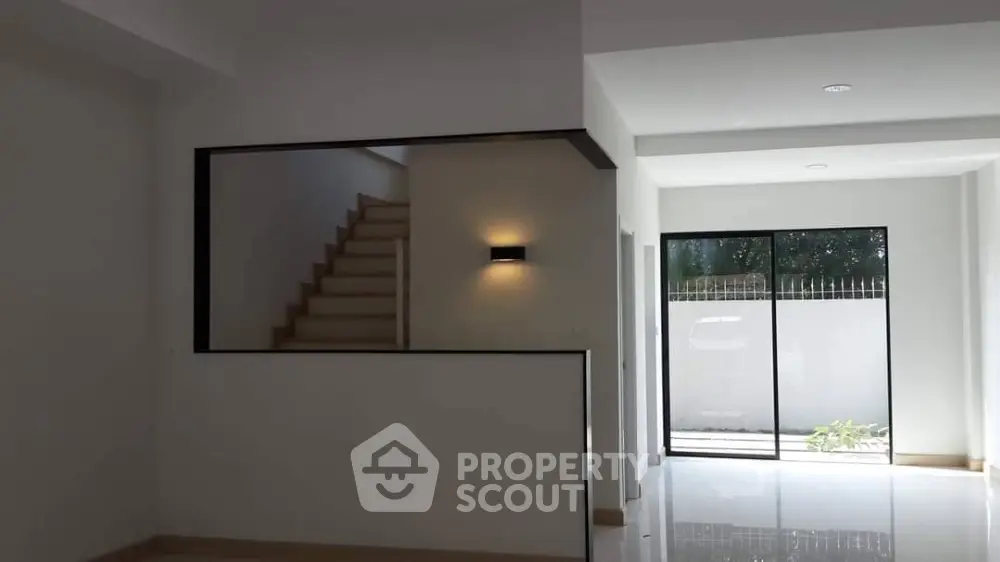 Spacious and modern living area with sleek staircase and abundant natural light from large glass doors leading to a serene outdoor space.