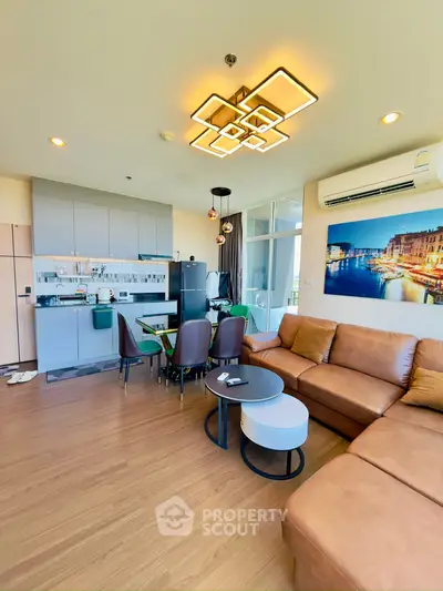 Modern open-layout living room with stylish furniture and kitchen area, featuring elegant lighting and wooden flooring.