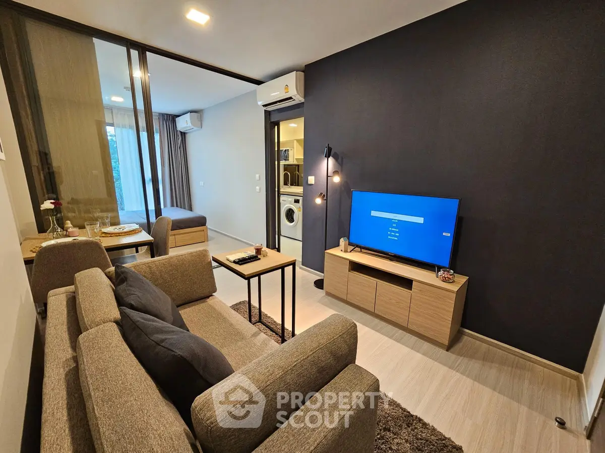 Modern living room with cozy seating, TV, and view into bedroom and kitchen area.