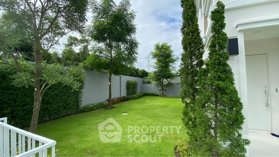 Spacious green garden with lush trees and modern white building exterior, perfect for outdoor relaxation.