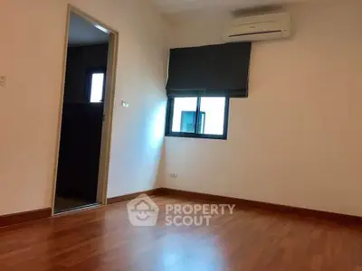Spacious bedroom with wooden flooring and air conditioning unit.