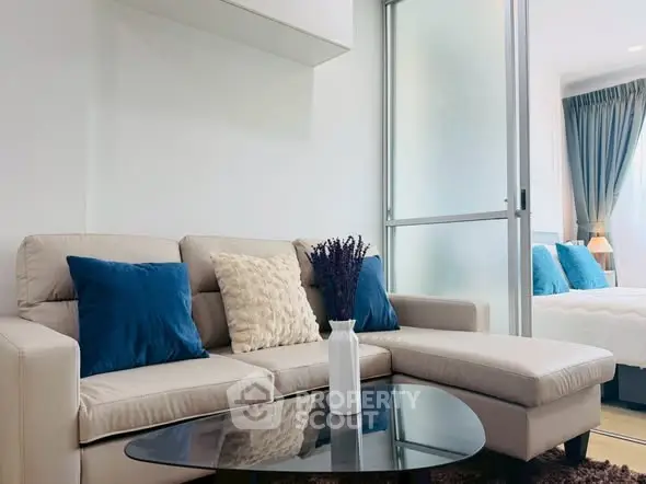 Modern living room with beige sectional sofa and blue cushions, adjacent to a cozy bedroom.