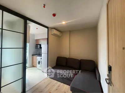 Modern living room with sliding doors and compact kitchen featuring washing machine and microwave.