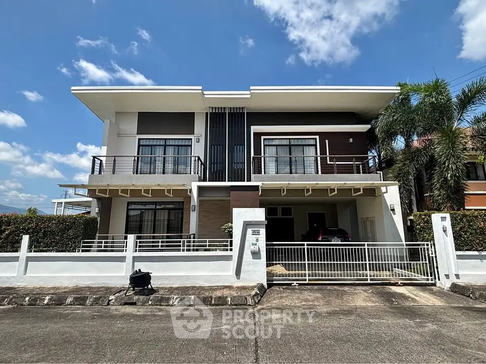 Modern two-story house with large windows and a gated driveway under a clear blue sky.