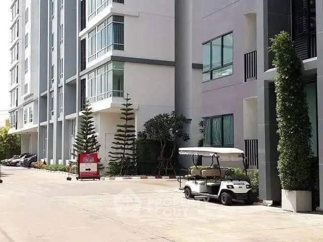 Modern apartment building exterior with landscaped greenery and golf cart parking.