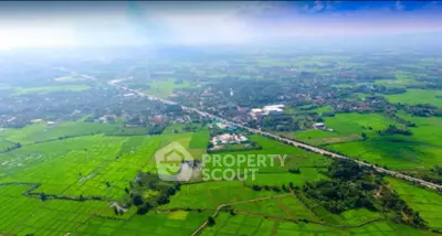 Aerial view of lush green fields and distant residential area, showcasing expansive rural landscape.