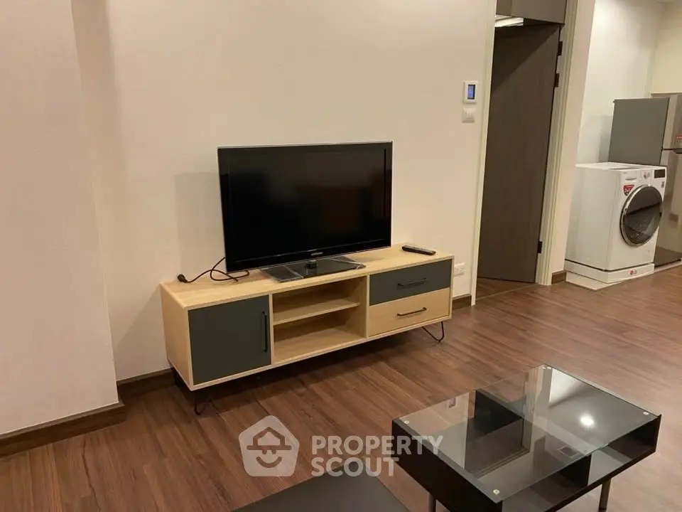 Modern living room with sleek TV stand and glass coffee table on wooden flooring.