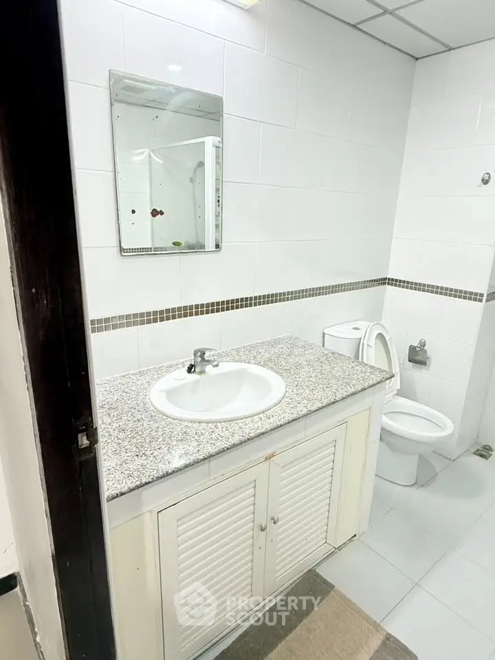 Modern bathroom with sleek white tiles and granite countertop in a stylish real estate property.