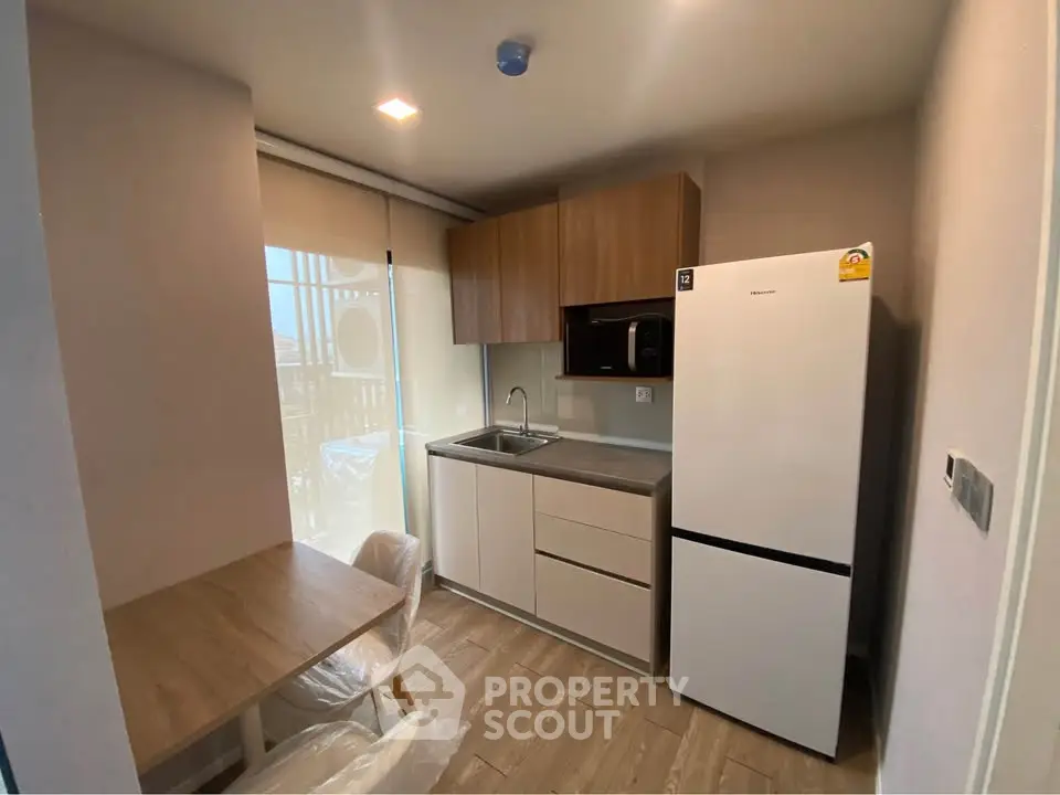 Modern compact kitchen with wooden cabinets, dining table, and large fridge in a cozy apartment.