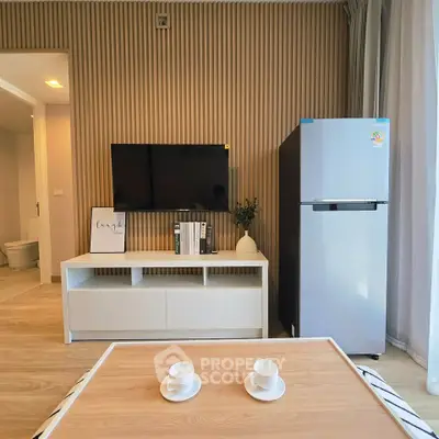 Modern living room with sleek TV setup and stylish decor, featuring a compact fridge and elegant wooden accents.