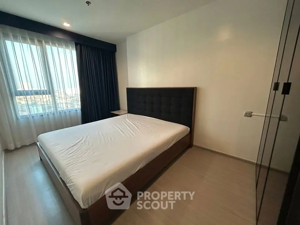 Spacious bedroom with large window and modern furnishings in a high-rise apartment.