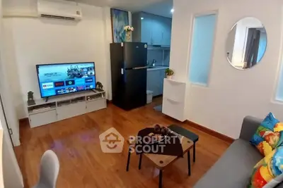Modern living room with TV, air conditioning, and compact kitchen area in a cozy apartment.