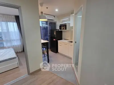 Modern apartment interior with kitchen and bedroom view, featuring sleek design and natural lighting.