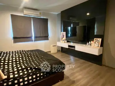 Modern bedroom with sleek black and white decor, featuring a large TV and stylish furnishings.