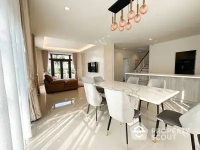 Elegant dining space with gleaming white marble floors, modern furniture, and chic copper pendant lights, seamlessly connected to a cozy living area.