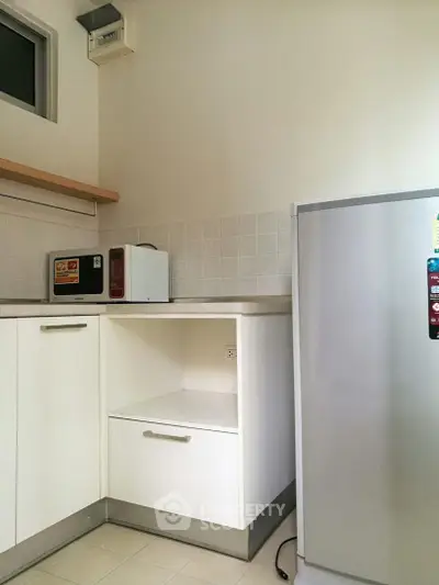 Modern kitchen with sleek white cabinets and appliances, featuring a microwave and refrigerator.
