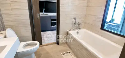 Modern bathroom with bathtub and view into sleek kitchen area.