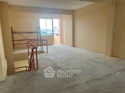 Spacious unfinished interior with large window and construction scaffolding, ideal for customization.