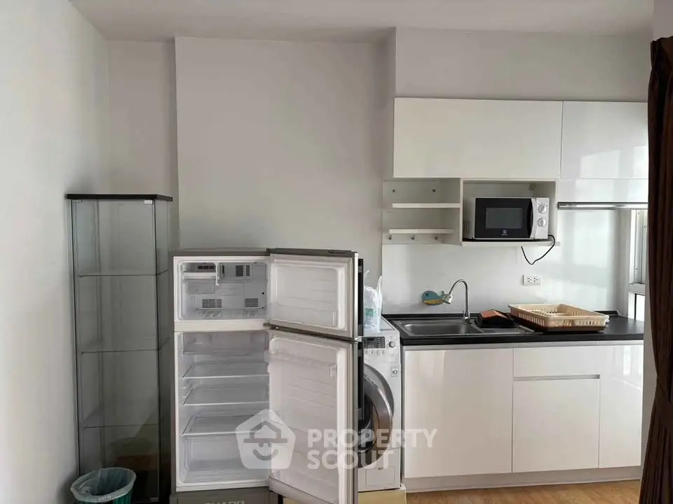 Modern kitchen with sleek cabinets, fridge, and washing machine in compact layout.