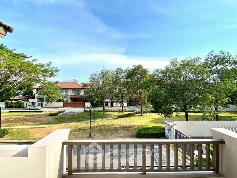 Charming residential view from balcony overlooking lush green park and suburban homes.