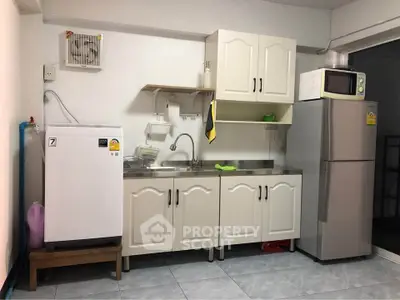 Compact kitchen with white cabinets, fridge, microwave, and washing machine in a cozy apartment.