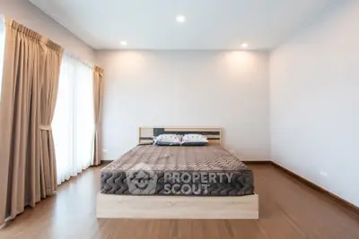 Spacious bedroom with large windows and elegant curtains, featuring a modern bed and wooden flooring.