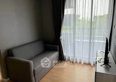 Cozy living room with modern sofa and TV, featuring a balcony view through sheer curtains.
